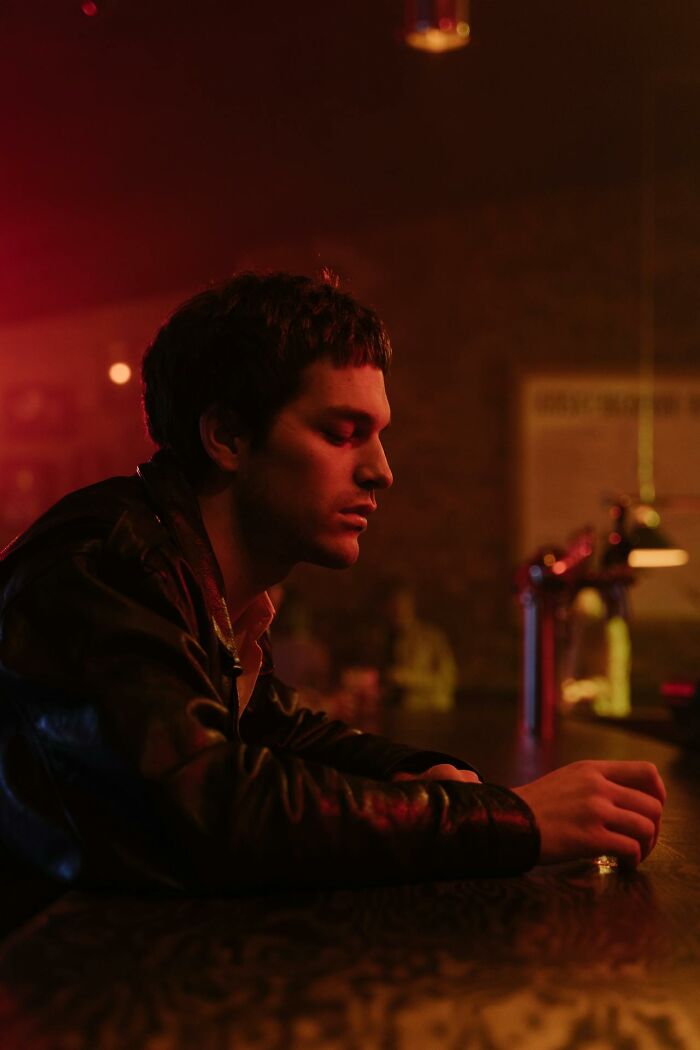 Young man sitting pensively at a bar in low red light, representing questions women would ask men without judgment.