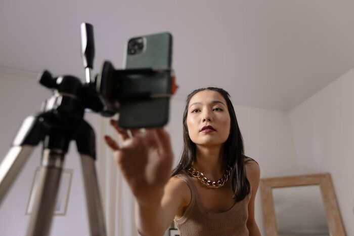 Young woman recording a video using smartphone on tripod, illustrating jobs that shouldn’t be earning as much as they do.
