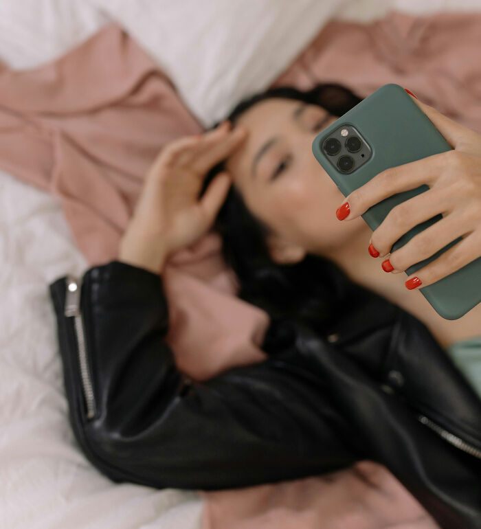 Woman with red nails holding smartphone, lying on bed, illustrating weird ways people earned quick money online.