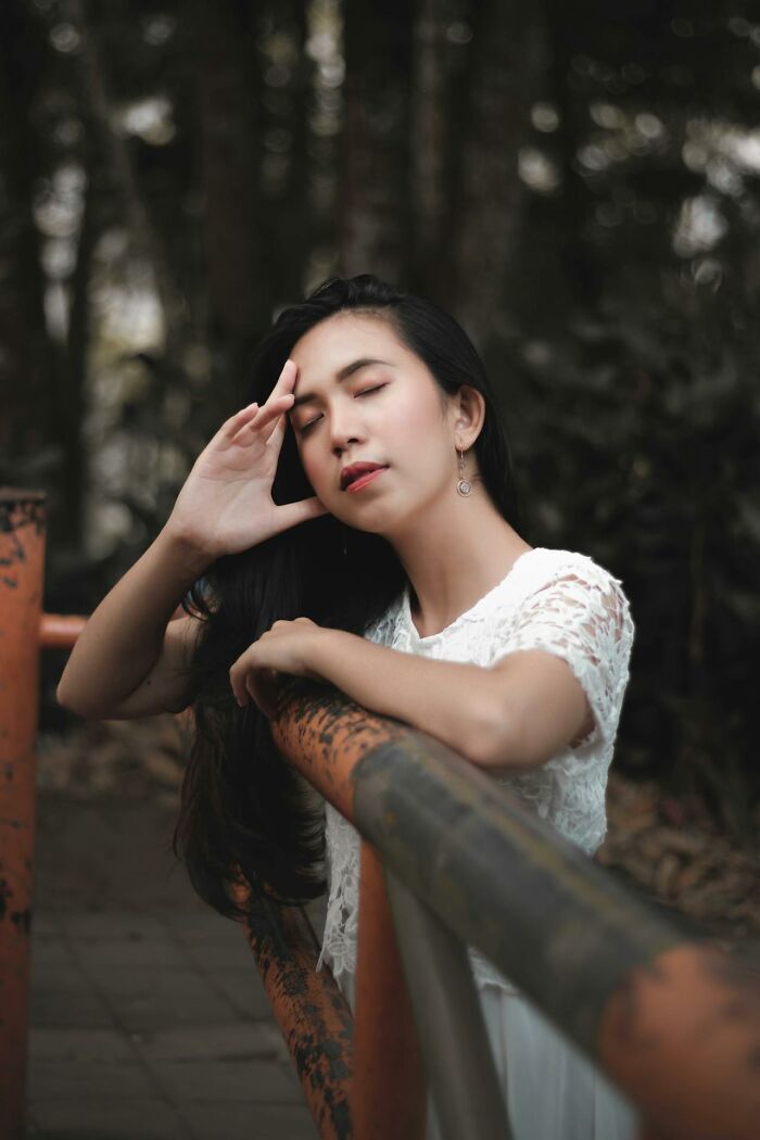 Young woman in white lace top leaning on rusted railing with eyes closed, reflecting on feeling instantly unsafe with a man.