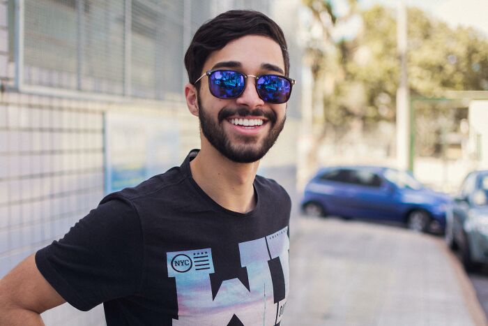 Young man smiling outdoors wearing sunglasses and a black shirt, illustrating cultural differences in a global setting.