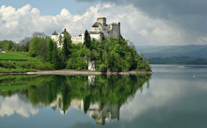 Historic castle surrounded by lush greenery reflected in calm water, representing national stereotypes and cultural charm.