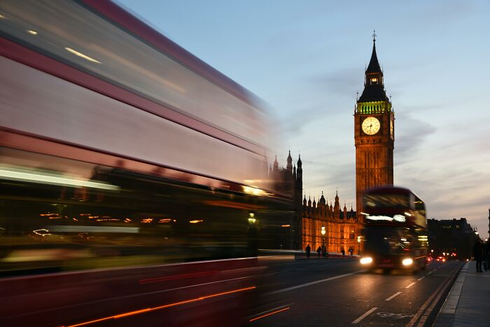Big Ben clock tower at dusk with iconic red double-decker buses in motion, a famous thing linked to the country quiz.