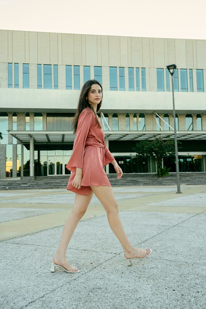 Young woman walking confidently outdoors in a coral outfit, representing women and microfeminisms in a modern urban setting.