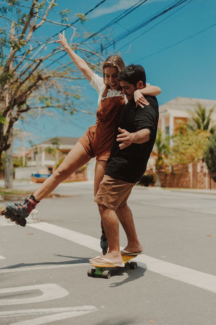 A woman and man enjoying outdoor fun with rollerblades and a skateboard, capturing women and men interaction.