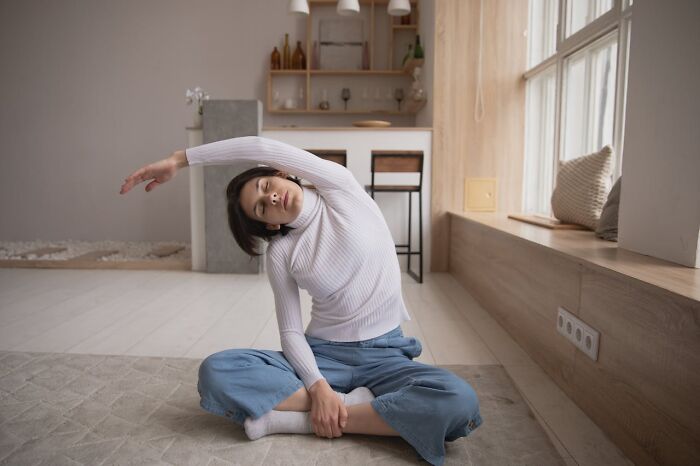 Young woman stretching indoors on the floor, enhancing her quality of life with mindful movement and relaxation practices.