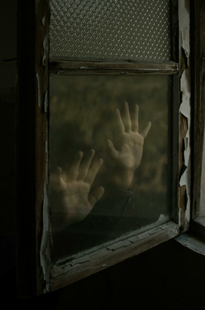 Hands pressed against a foggy, c*****d window in a dark, eerie room depicting a haunting feeling linked to serotonin syndrome.