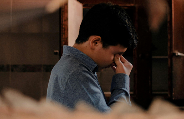 Man in blue shirt showing emotional distress, reflecting on grandbaby as a sign from late wife in a dimly lit room.