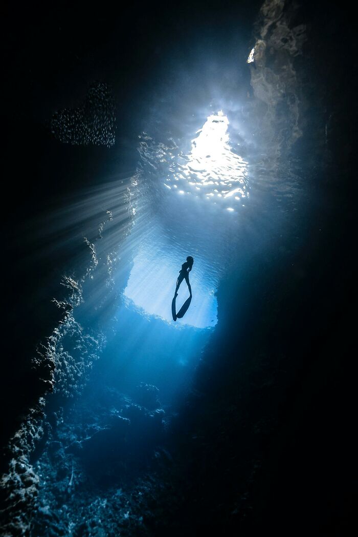 A lone diver illuminated by beams of light in a deep underwater cave, evoking mystery related to serotonin syndrome.