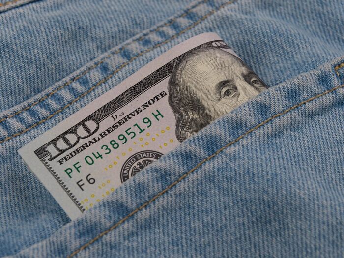 One hundred dollar bill partially peeking out of denim jeans pocket in a shocking real-life moment.