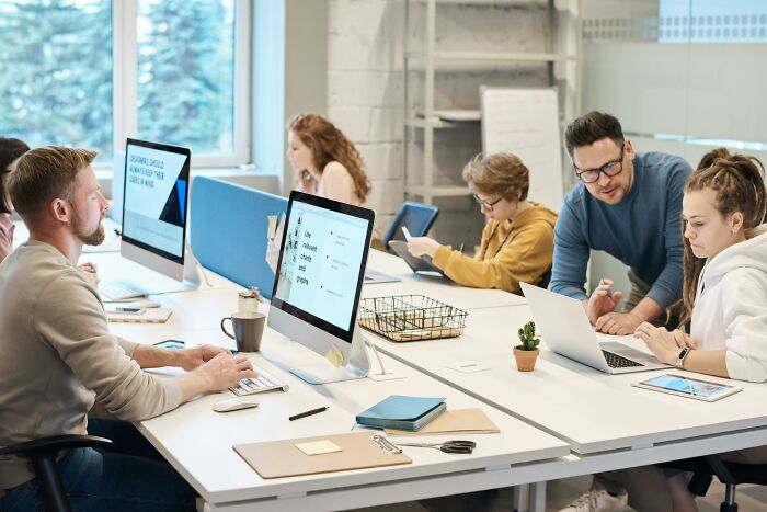 A group of young professionals working at computers in a modern office, illustrating Gen X balancing technology and teamwork.