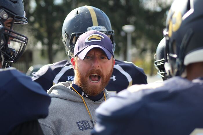 Football coach shouting instructions to players on the field, illustrating jobs that shouldn’t be earning as much as they do.