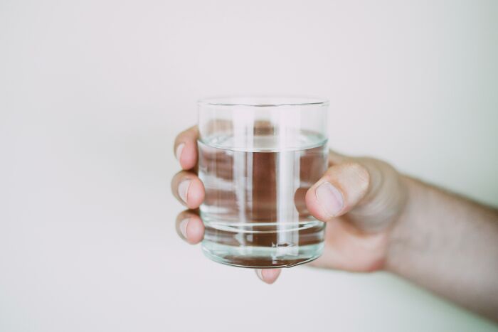 Hand holding a clear glass filled with water against a plain white background, tech guys found weird disturbing.