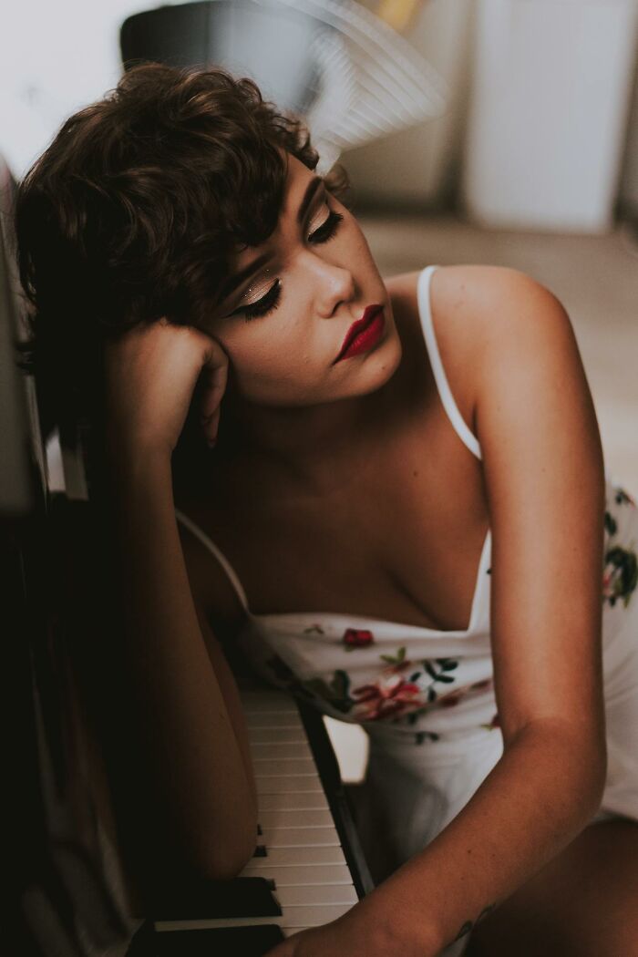 Woman with short curly hair and red lipstick leaning on a piano, reflecting on moments she felt instantly unsafe with a man.