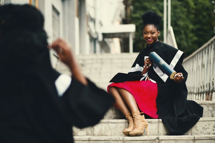 Young woman in graduation gown sitting on stairs holding diploma, reflecting on absurd things told growing up.