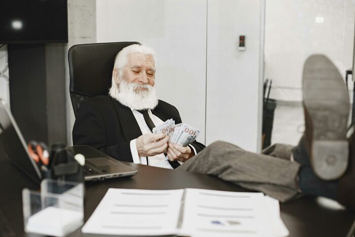 Elderly man in suit counting money at office desk, illustrating absurd things people were told growing up.