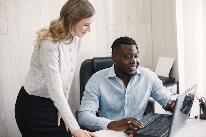 Two coworkers using laptop together in an office, demonstrating real-life cheat codes for productivity.