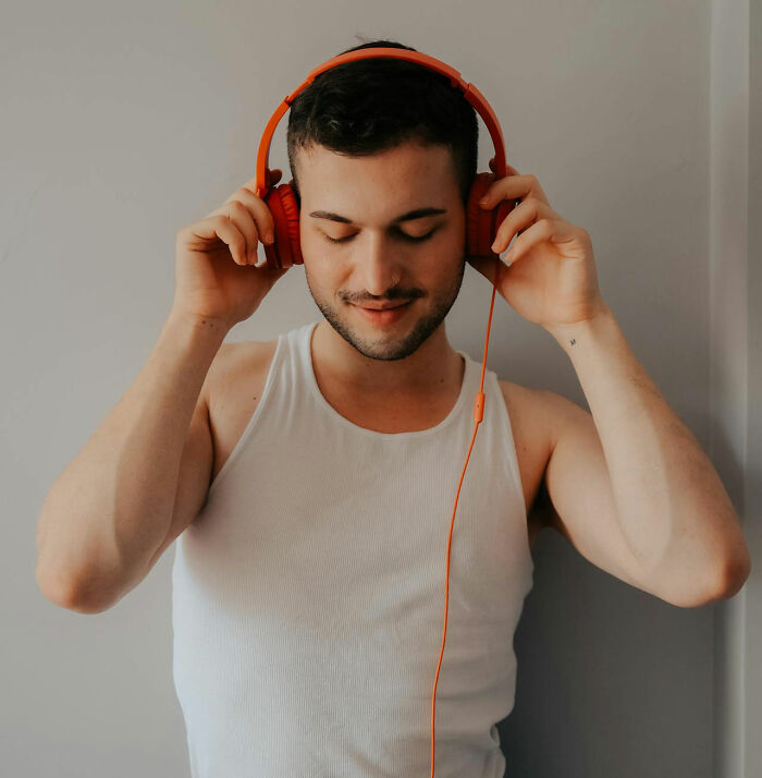Young man enjoying music with orange headphones, reflecting improved quality of life and personal happiness.