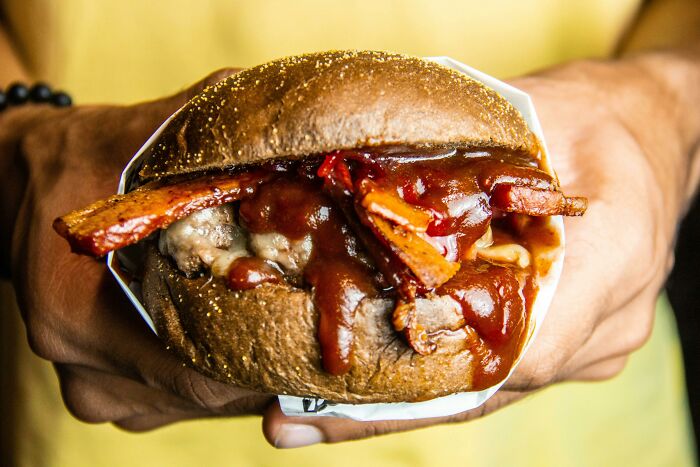 Close-up of a bacon sandwich with barbecue sauce held in hands, highlighting hilarious and weird things found secretly.