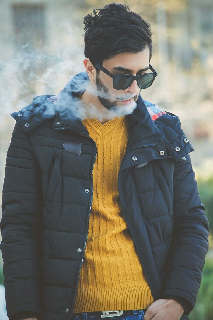 Young man in sunglasses and winter jacket breathing out smoke, symbolizing lifestyle changes that improve quality of life.