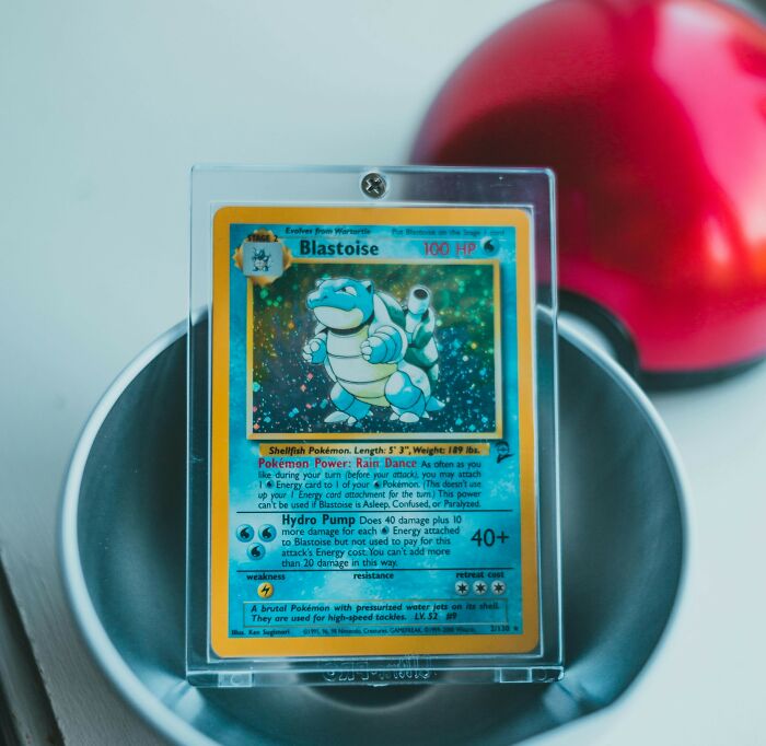 A rare Blastoise Pokémon card in a protective case with a Poké Ball in the background, symbolizing wildest life blunders.