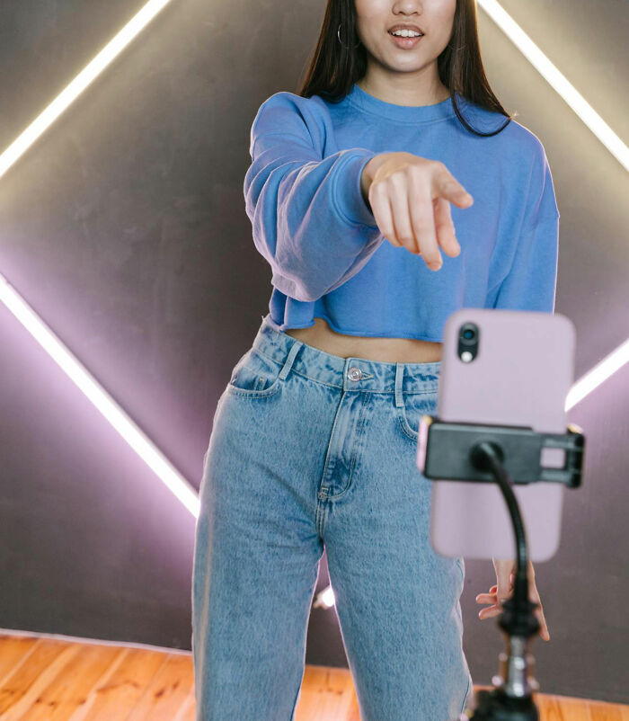 Young woman recording video on smartphone, illustrating challenges the middle class and Gen Z face today.