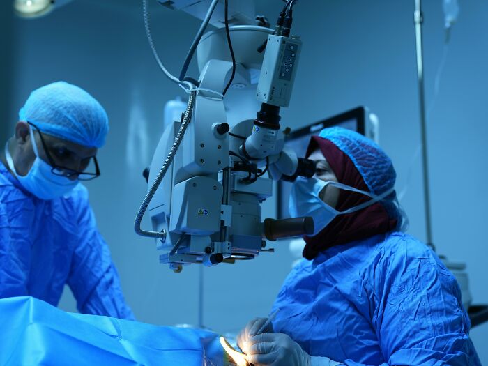 Two plastic surgeons in surgical gear performing a procedure using advanced medical equipment in an operating room.
