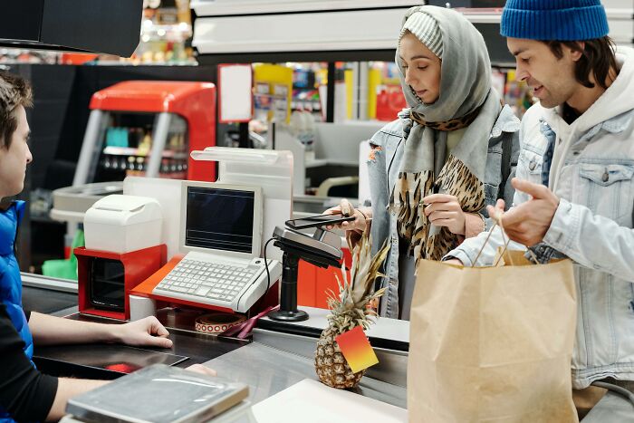 Couple at grocery checkout using mobile payment while cashier looks on, illustrating employees sharing strange recruiter stories.