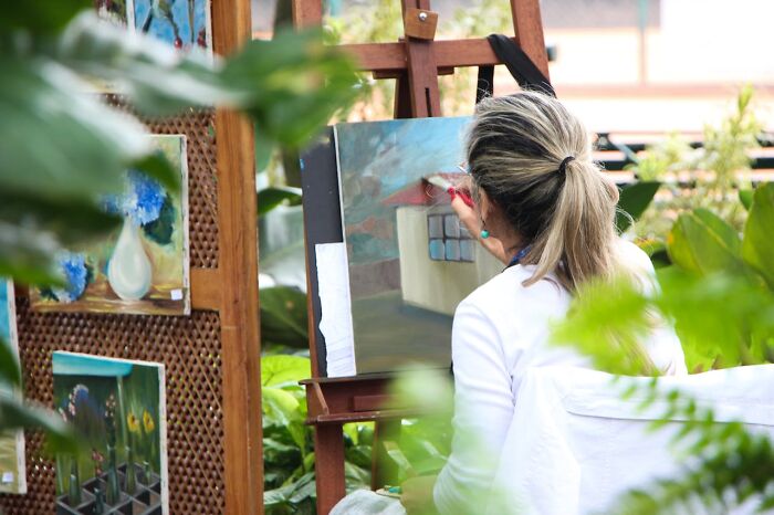 Female artist painting a house outdoors surrounded by plants, revealing industry secrets behind closed doors.