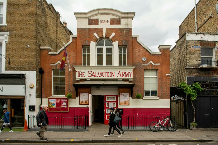 People share concerns near The Salvation Army building on a city street with pedestrians walking by.