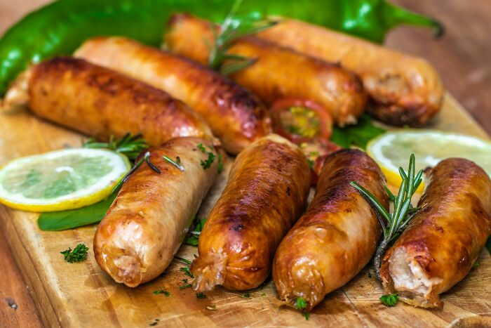 Grilled sausages on a wooden board garnished with lemon slices and green herbs, capturing a behind the tap vibe.