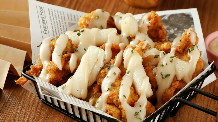 Basket of crispy fried chicken strips topped with creamy sauce and sprinkled with herbs, showcasing wild cooking opinions.