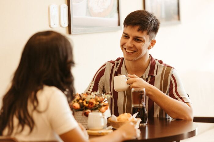 Man smiling and holding a coffee cup while talking to a woman, highlighting moments women felt instantly unsafe with a man.