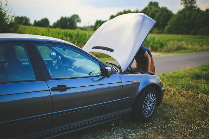 Person inspecting broken-down car on roadside, illustrating people share companies bad list concerns with vehicle issues.