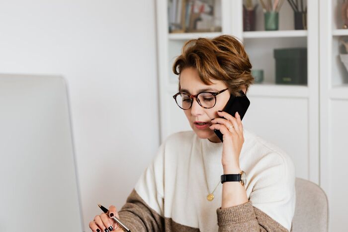 Person with glasses talking on phone while working at desk, representing jobs earning more than expected online.