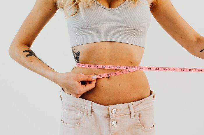 Woman measuring her waist with a tape measure representing improved quality of life through health and fitness habits.