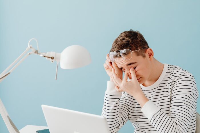 Young man rubbing eyes at his desk with laptop and lamp, reflecting on improving quality of life changes.