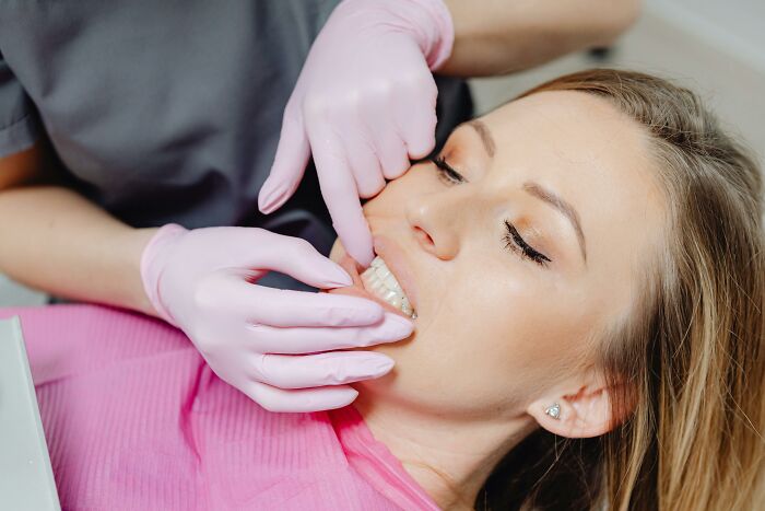 Dentist wearing pink gloves fitting dental braces on a woman’s teeth, symbolizing harsh life advice about challenges and growth.