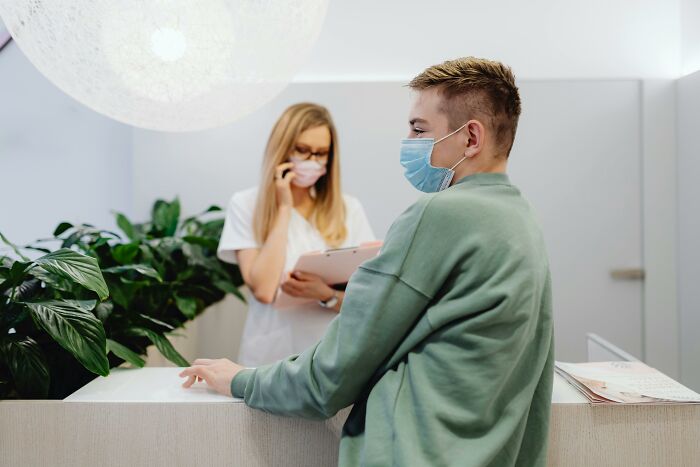 Patient wearing a mask consulting at the front desk of a clinic with a medical professional discussing cosmetic procedures.