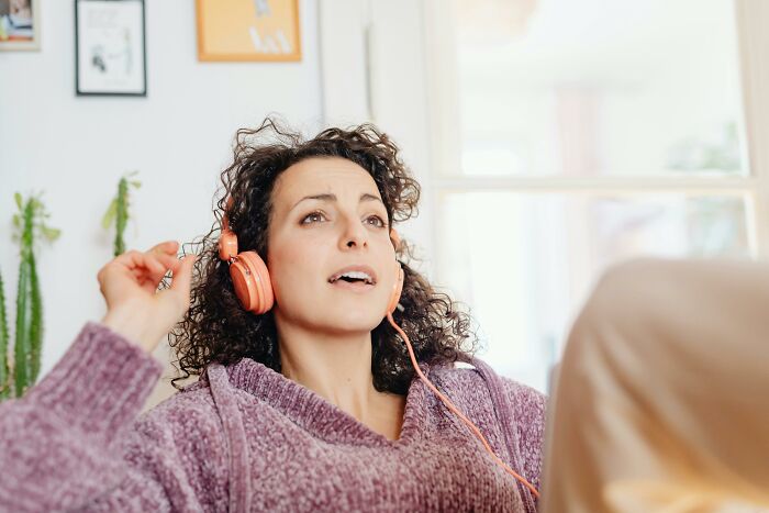 Woman with curly hair wearing orange headphones and a purple sweater experiencing placebo effect in real life at home.