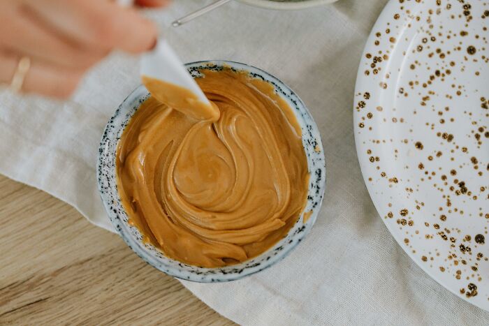 Smooth peanut butter being scooped from a bowl highlighting common foods that go bad quickly and raw milk risks.