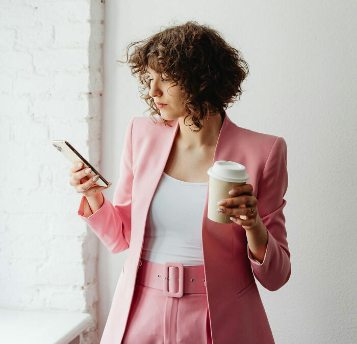Woman in a pink suit holding coffee and phone, illustrating unhinged things teachers say or do that actually work