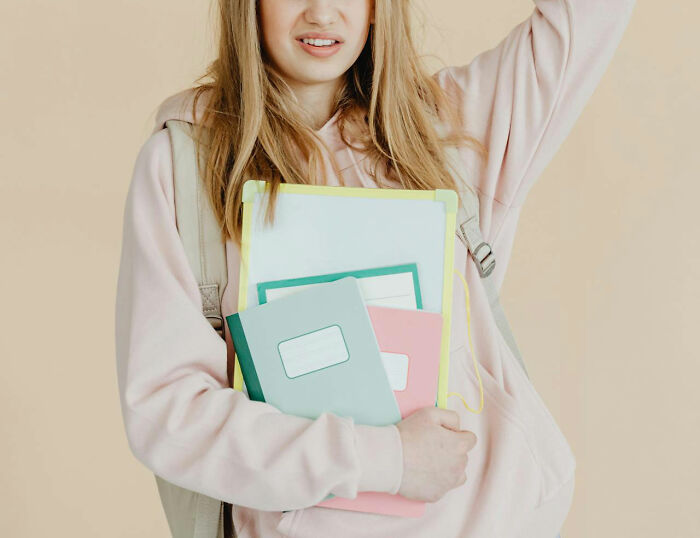 Young woman holding notebooks and a whiteboard with a hesitant expression, illustrating unhinged teacher habits that work.