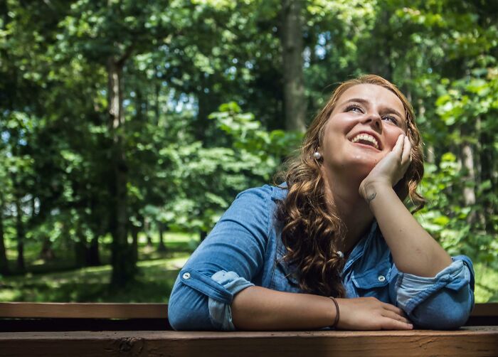 Young woman in blue shirt smiling and looking up thoughtfully outdoors, illustrating appalling facts people unaware concept.