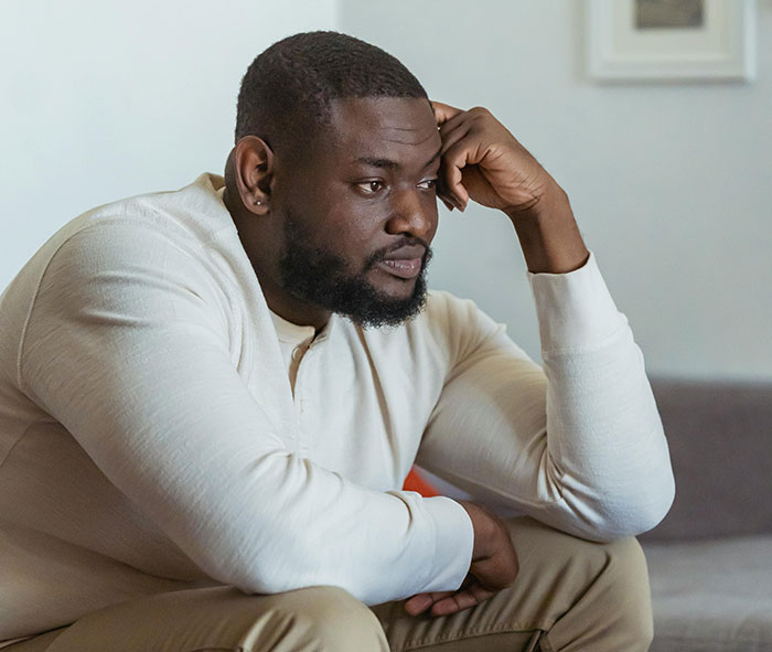 Man sitting indoors looking worried and thoughtful after family chaos and cigarettes brought inside by brother&rsquo;s girlfriend