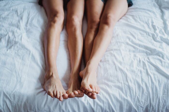 Two women lying side by side on a bed showing their legs and feet, representing questions women ask men.