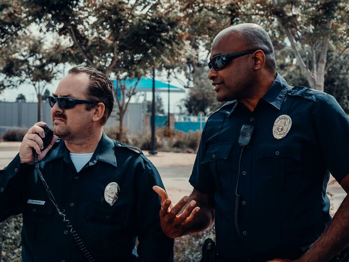 Two police officers wearing sunglasses and uniforms talk outdoors near trees, highlighting appalling facts people unaware.
