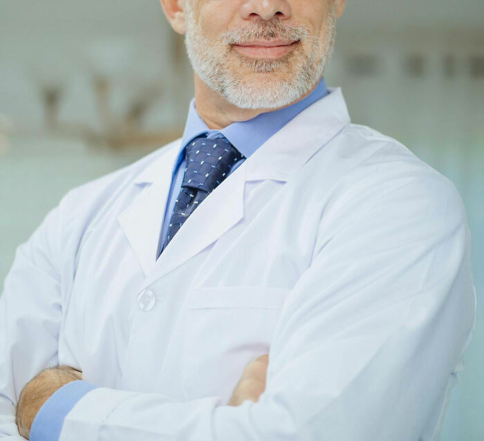 Middle-aged man in a white coat and tie standing with arms crossed, conveying a sense of safety and trust.