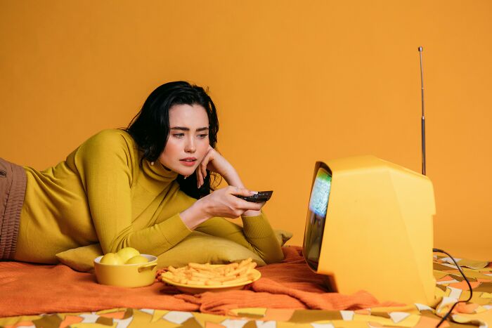 Young woman in a mustard sweater watching vintage TV, testing her knowledge of pop culture history facts at home. Young woman in a mustard sweater watching vintage TV, testing her knowledge of pop culture history facts at home.