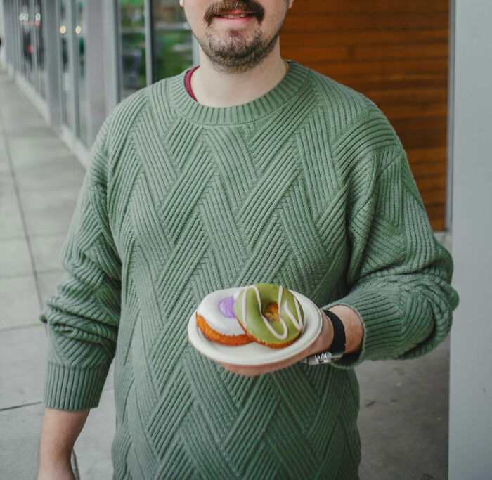 Man wearing green sweater holding two donuts on a plate, with a focus on feeling instantly unsafe with a man.